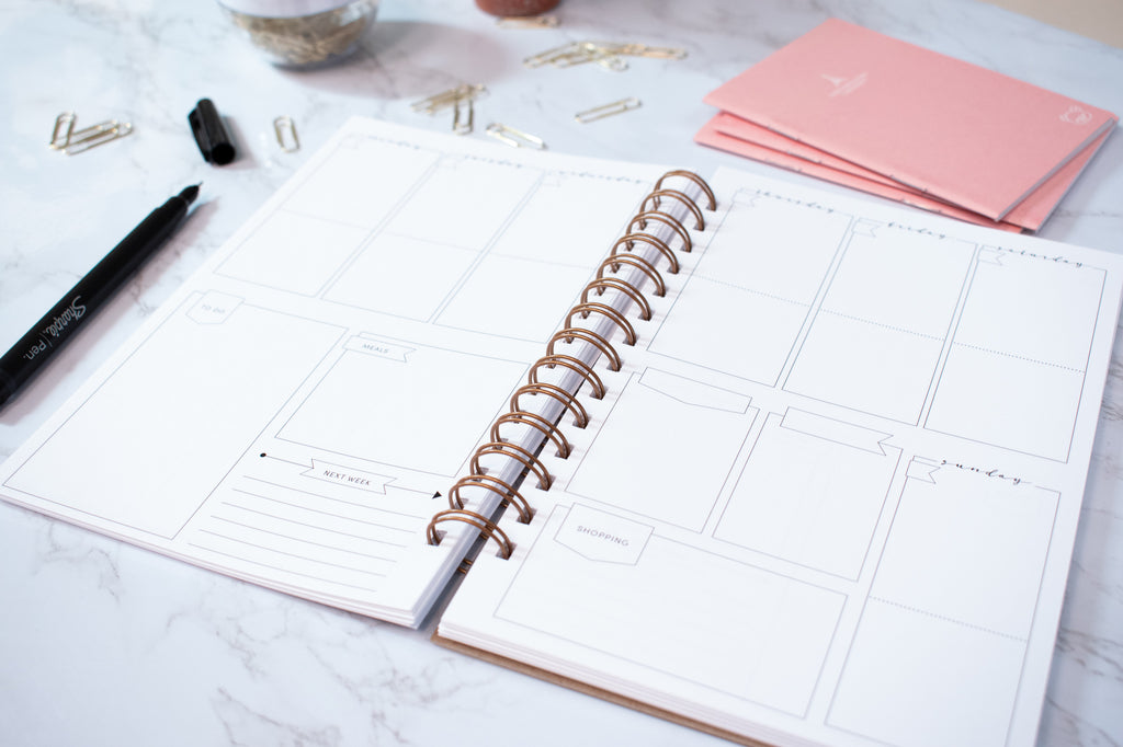 weekly planner pages in a wire spiral bound notebook for our customized planners sitting on a marble table with small pink notebooks next to it