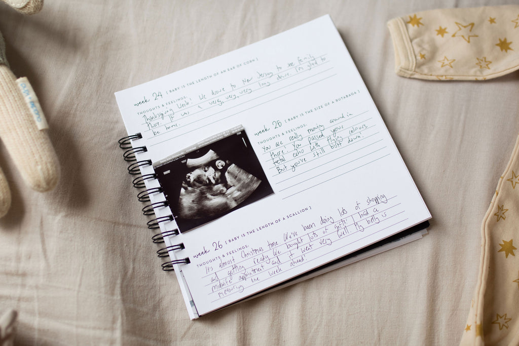 inside weekly journaling pages for pregnancy journal book to track pregnancy week by week with pictures of baby and belly and journaling space sitting on bed surrounded by baby clothes