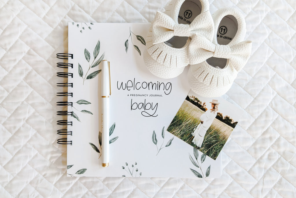pregnancy journal book to track pregnancy week by week with pictures of baby and belly and journaling space sitting on white quilt with baby shoes and pregnant woman photo