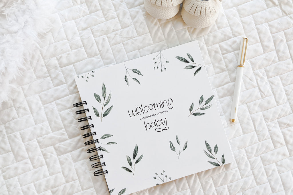 pregnancy journal book to track pregnancy week by week with pictures of baby and belly and journaling space sitting on white quilt with baby shoes 